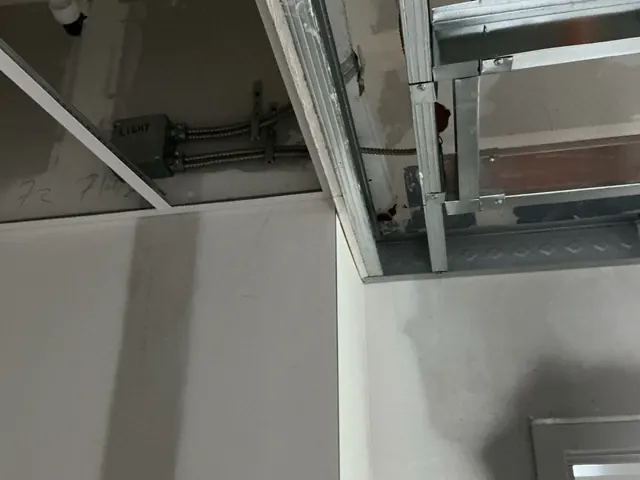 Metal conduit running to a gray junction box above a partly installed suspended ceiling grid during rough-in