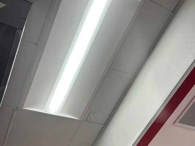Single long LED troffer fixture lit in a white drop-ceiling grid, restaurant interior